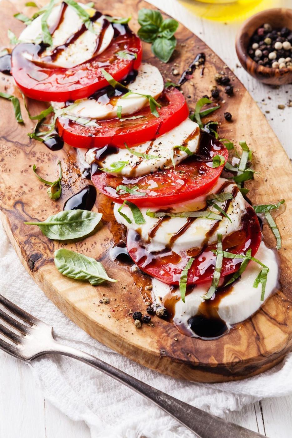 Caprese mit Tomaten, Mozzarella, Basilikum und Balsamico auf dem Holzbrett